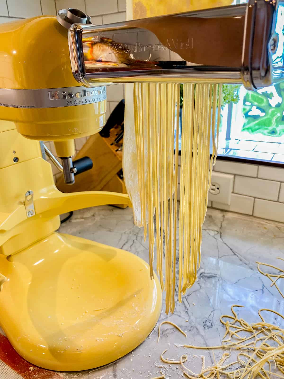 KitchenAid stand mixer with a pasta attachment with spaghetti noodles being made.