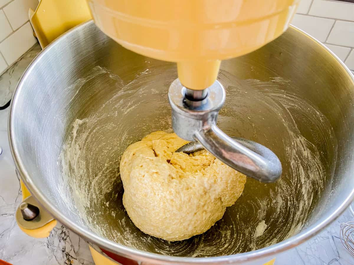 Yellow KitchenAid stand mixer with a dough hook with dough in the bowl.