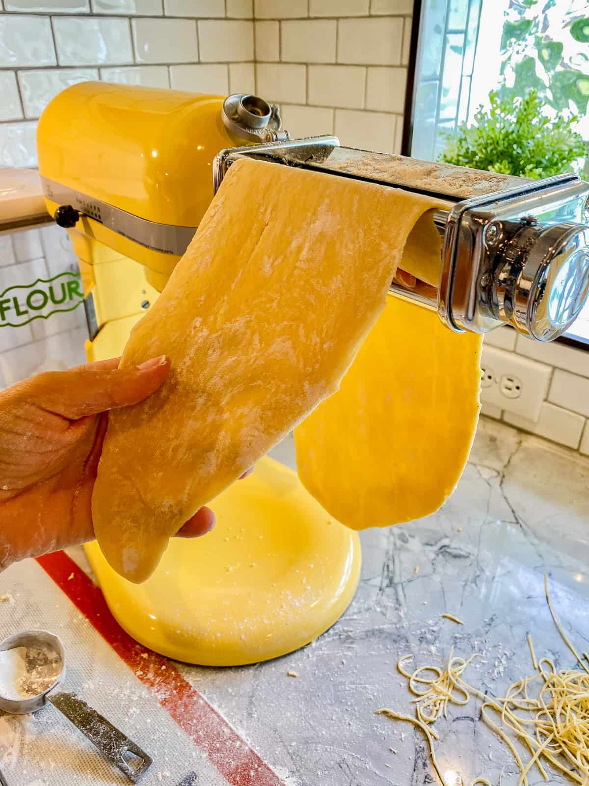 Hand holding dough through a KitchenAid Pasta attachment.