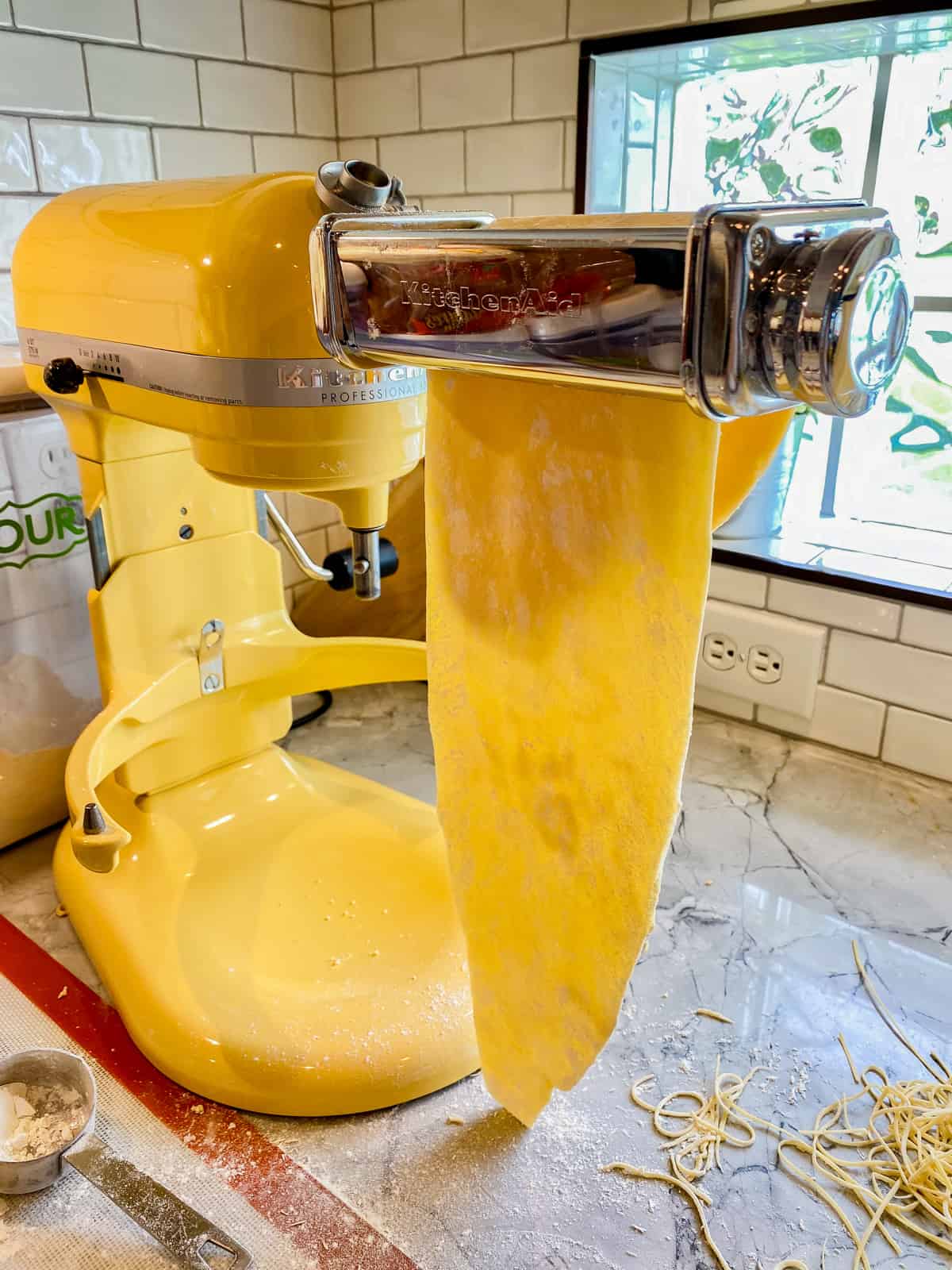 KitchenAid mixer with pasta attachment and dough going through it.