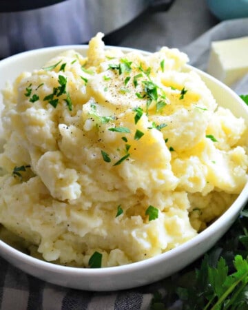 White bowl with fluffy mashed potatoes topped with butter and parsley.