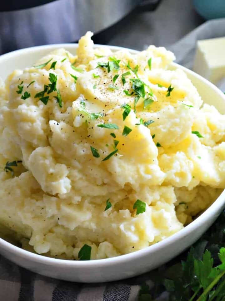 White bowl with fluffy mashed potatoes topped with butter and parsley.