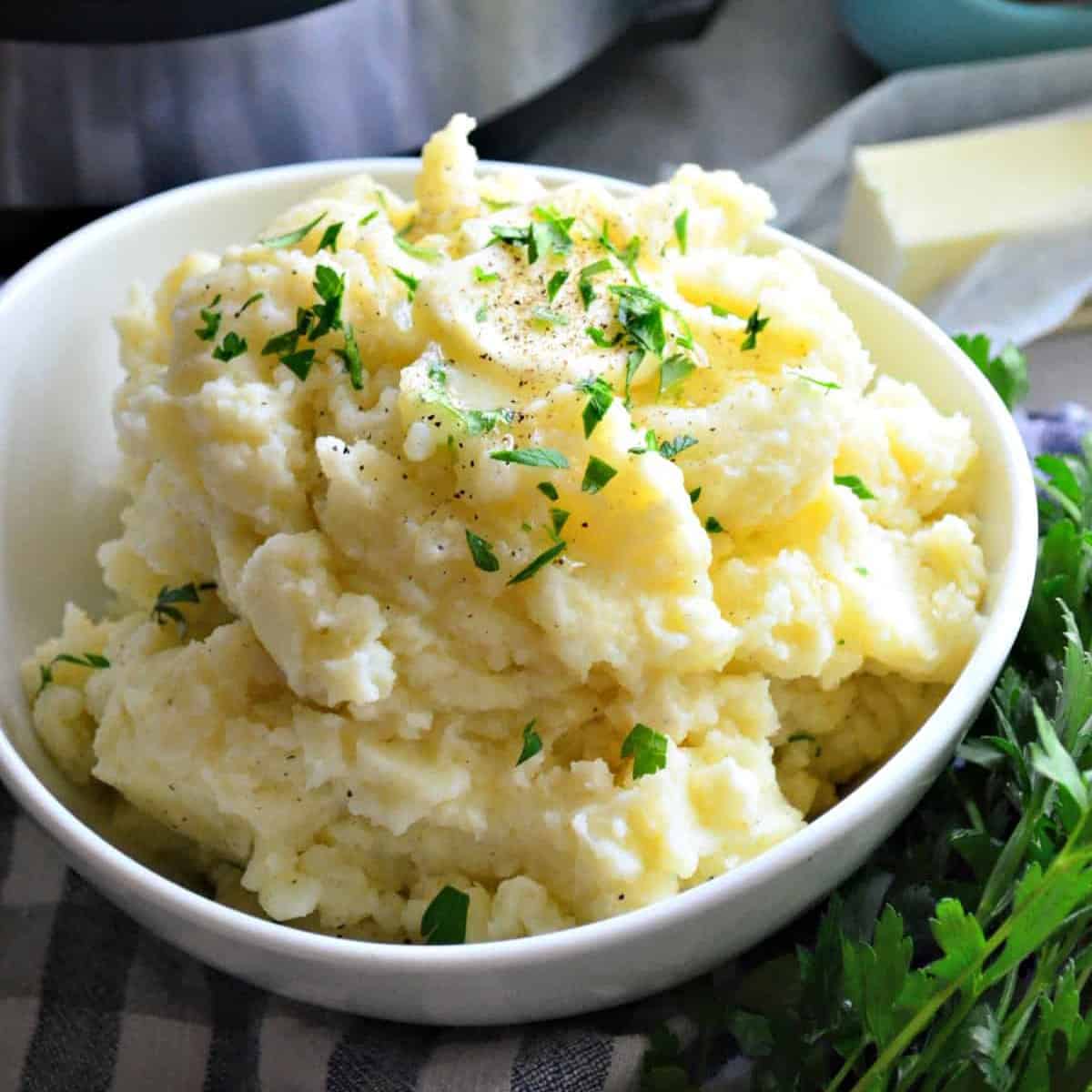 White bowl with fluffy mashed potatoes topped with butter and parsley.