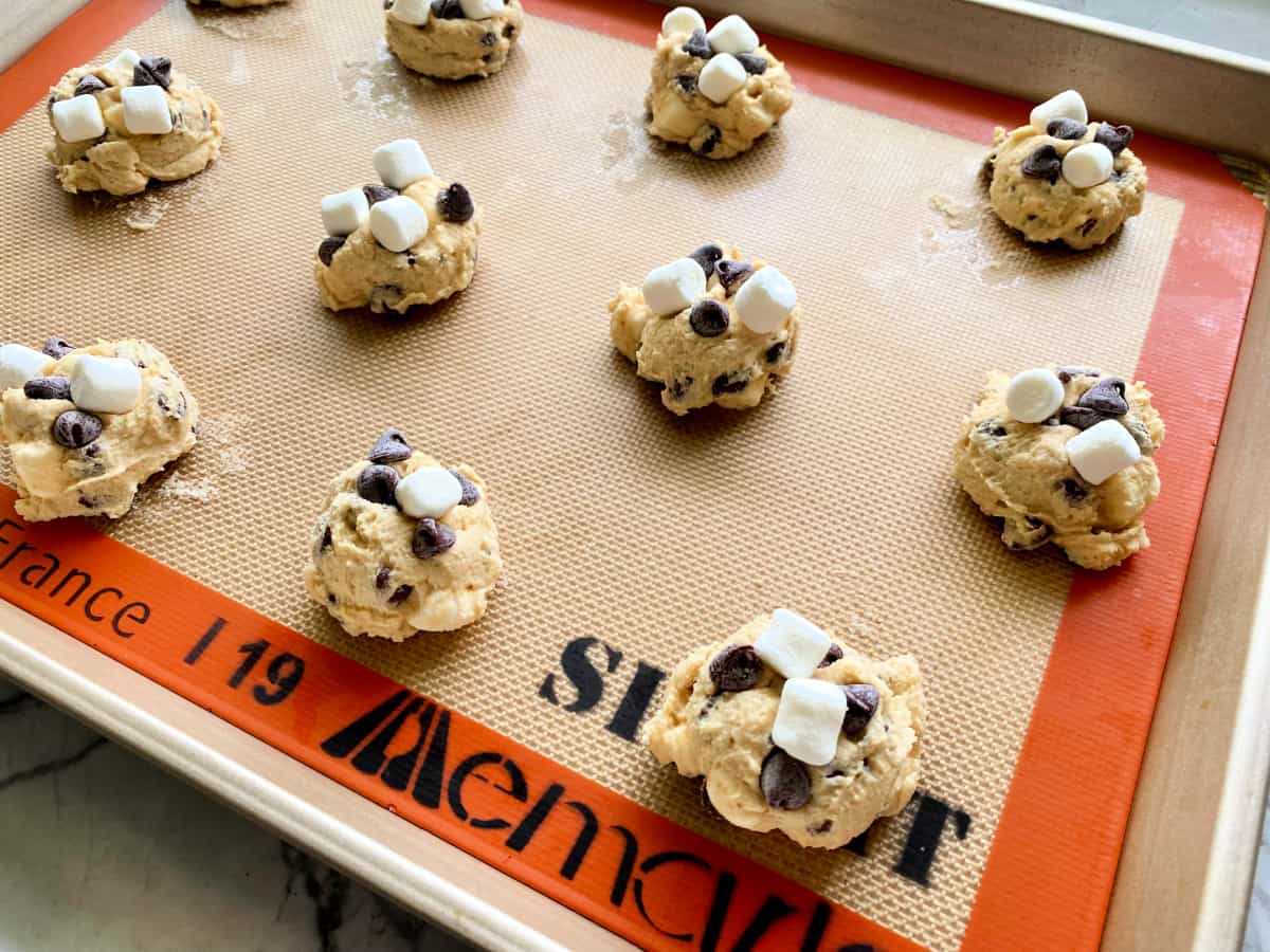 Gold baking sheet with scooped raw cookie doubgh on an orange silpat.