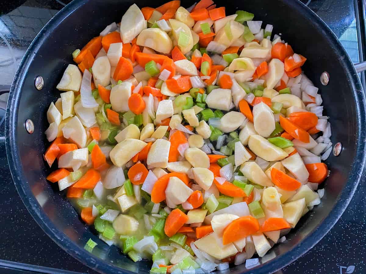 Black skillet filled with carrots, onions, celery, and parsnips chopped.