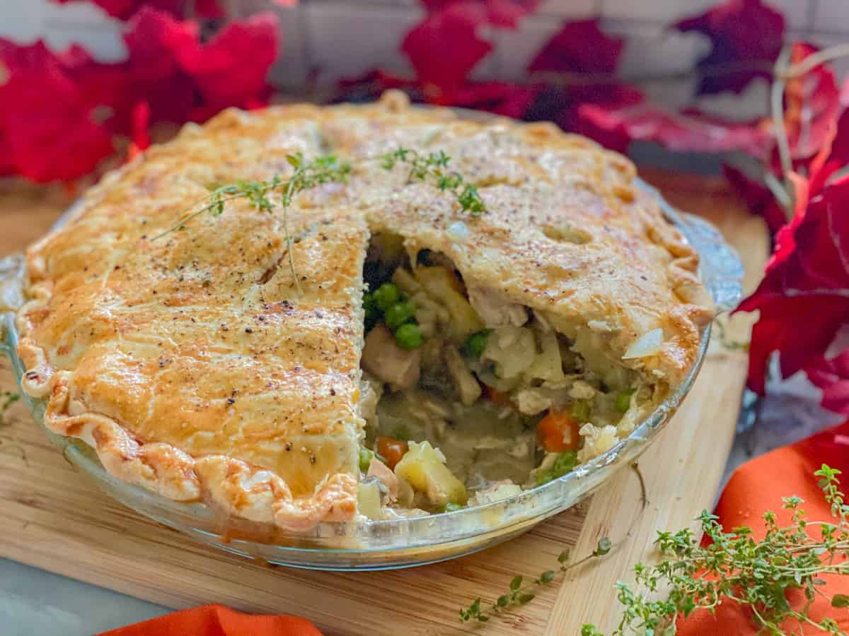 Glass pie plate with a turkey pot pie resting on a wood cutting board.