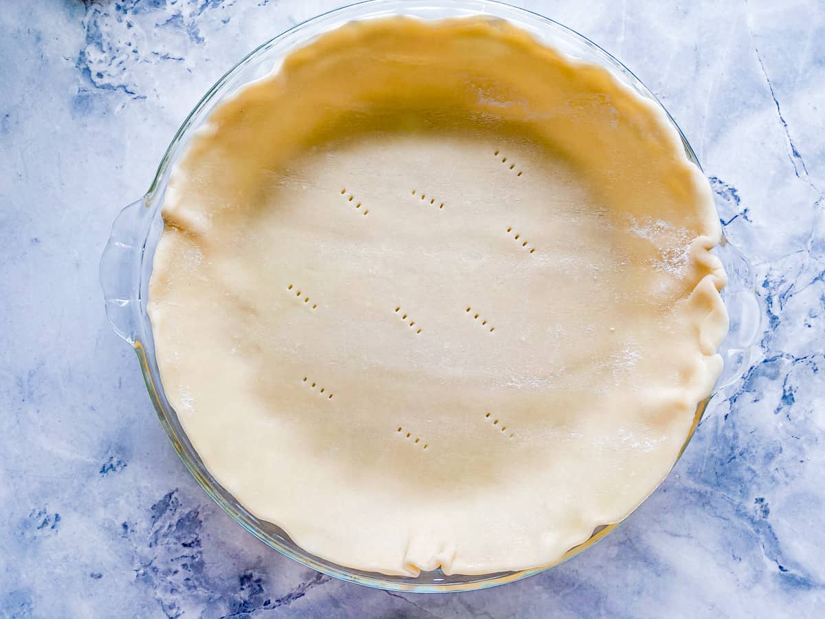 Glass pie plate with pie crust on top with fork tines pricked all over.