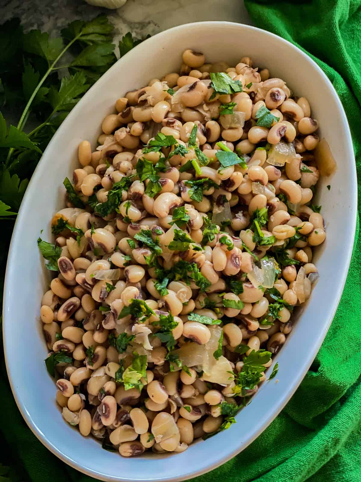 Cooked black eyed peas with fresh herbs resting in a white oval bowl.