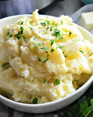 White bowl with fluffy mashed potatoes topped with butter and parsley.