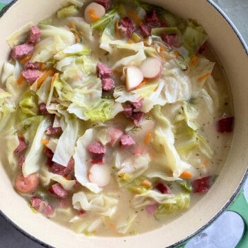Large green pot filled with cabbage, sausage, potatoes, and broth on a marble countertop.