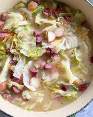 Large green pot filled with cabbage, sausage, potatoes, and broth on a marble countertop.