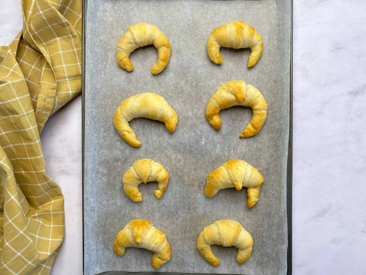 Parchment lined baking sheet with cooked crescent rolls on it.