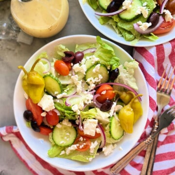 Square photo of 2 bowls of greek salad with a red and white striped napkin.