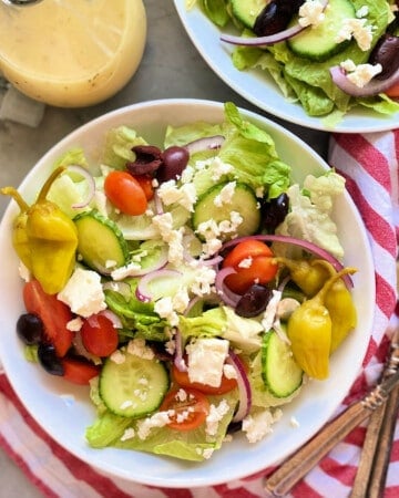 Square photo of 2 bowls of greek salad with a red and white striped napkin.