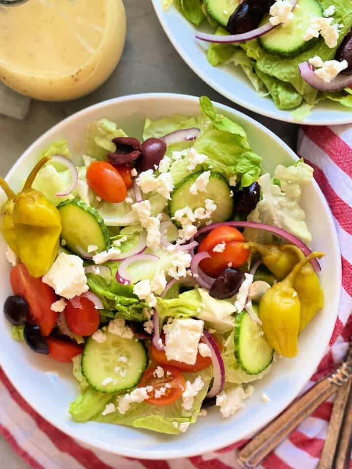 Square photo of 2 bowls of greek salad with a red and white striped napkin.