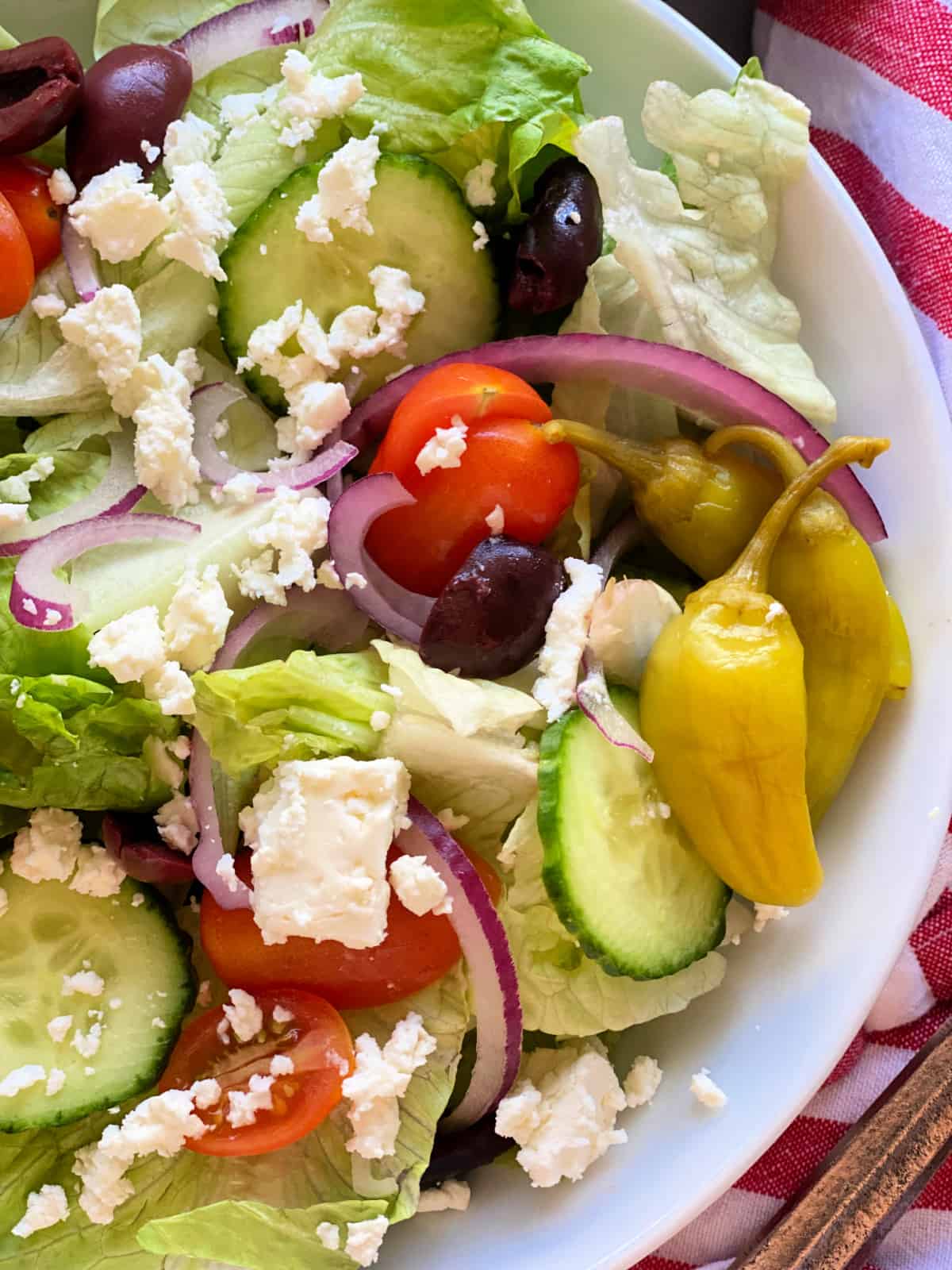 White bowl with lettuce, tomato, pepperorcini, onion, and feta.