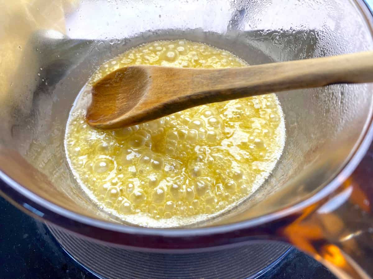 Glass pot with sugar butter mixture with a wooden spoon.