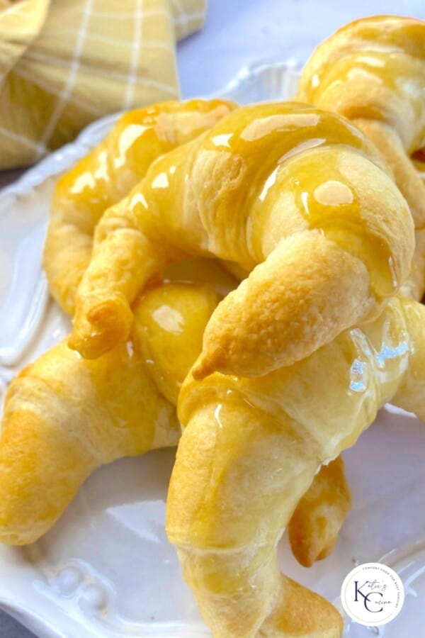 Glazed croissants on a white platter with a logo on the right corner.