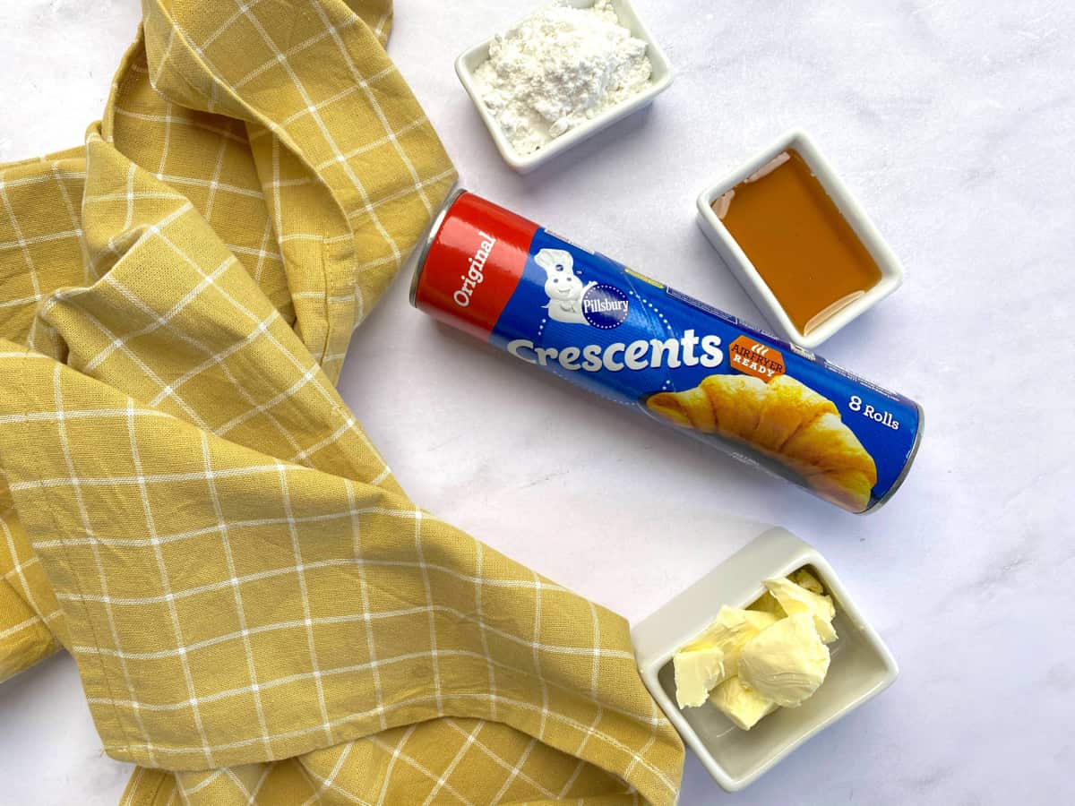 Ingredients on marble countertop: crescent rolls, butter, honey, and powder sugar.