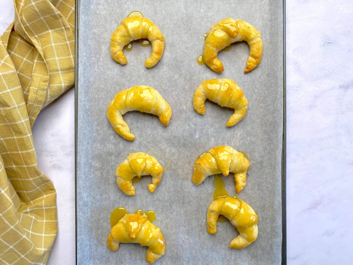 Parchment lined baking sheet with cooked crescent rolls with glaze on it.