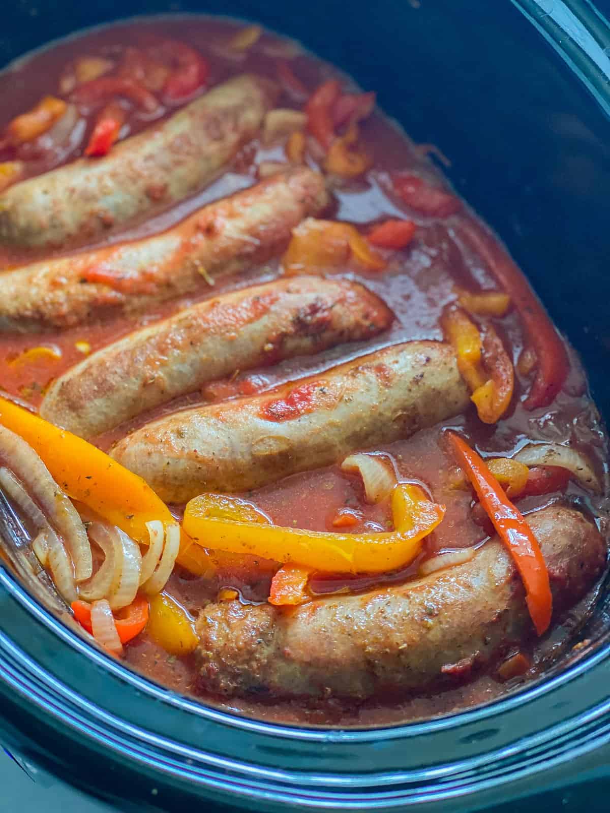 Picture of Italian Sausages inside of an Instant Pot marinating with bell peppers, onions, and marinara sauce, taken from an up close angle.