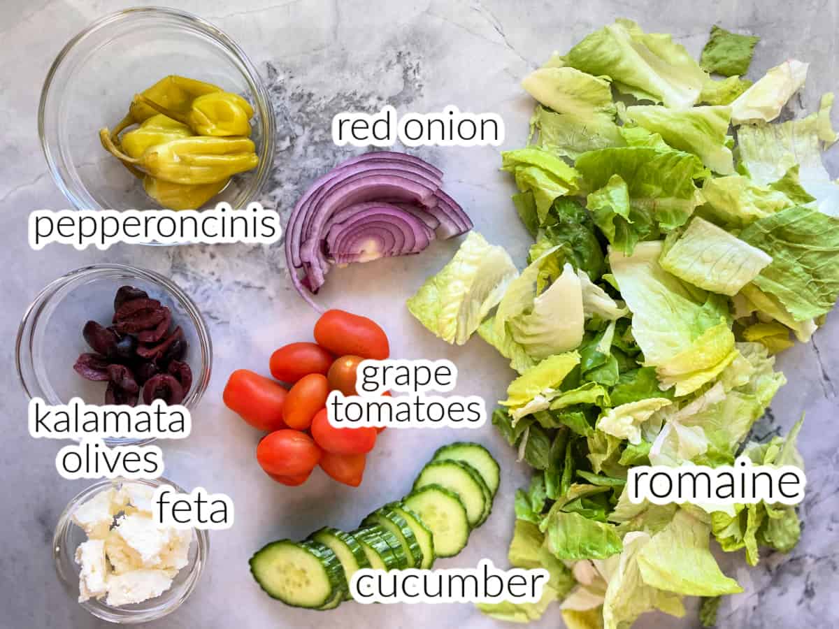 Ingredients on counter: romaine, cucumber, tomatoes, red onions, kalamata olives, feta, and pepperoncinis.