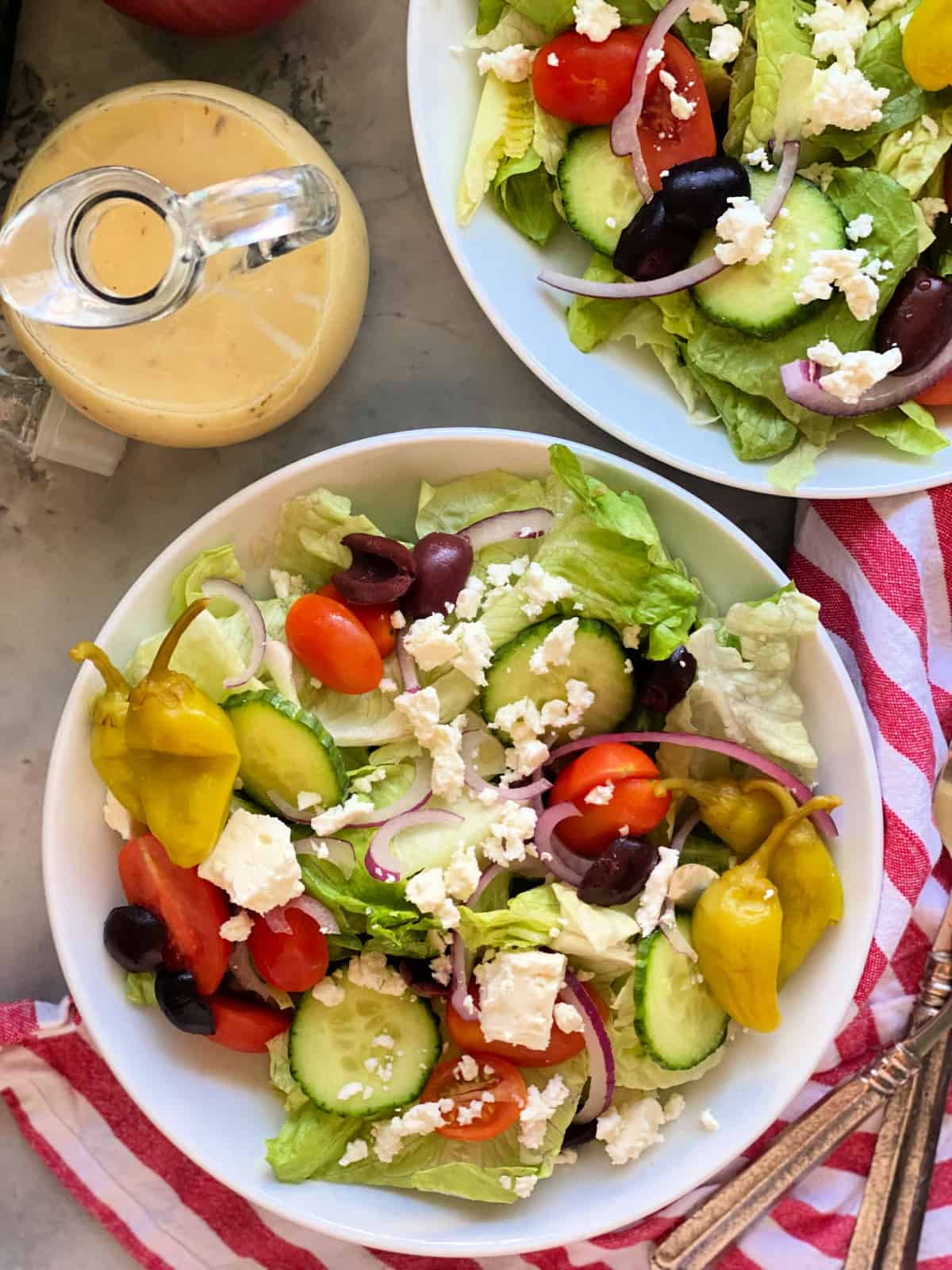 White circle bowls filled with lettuce, cucumber, tomatoes, onions, feta with dressing on the side.