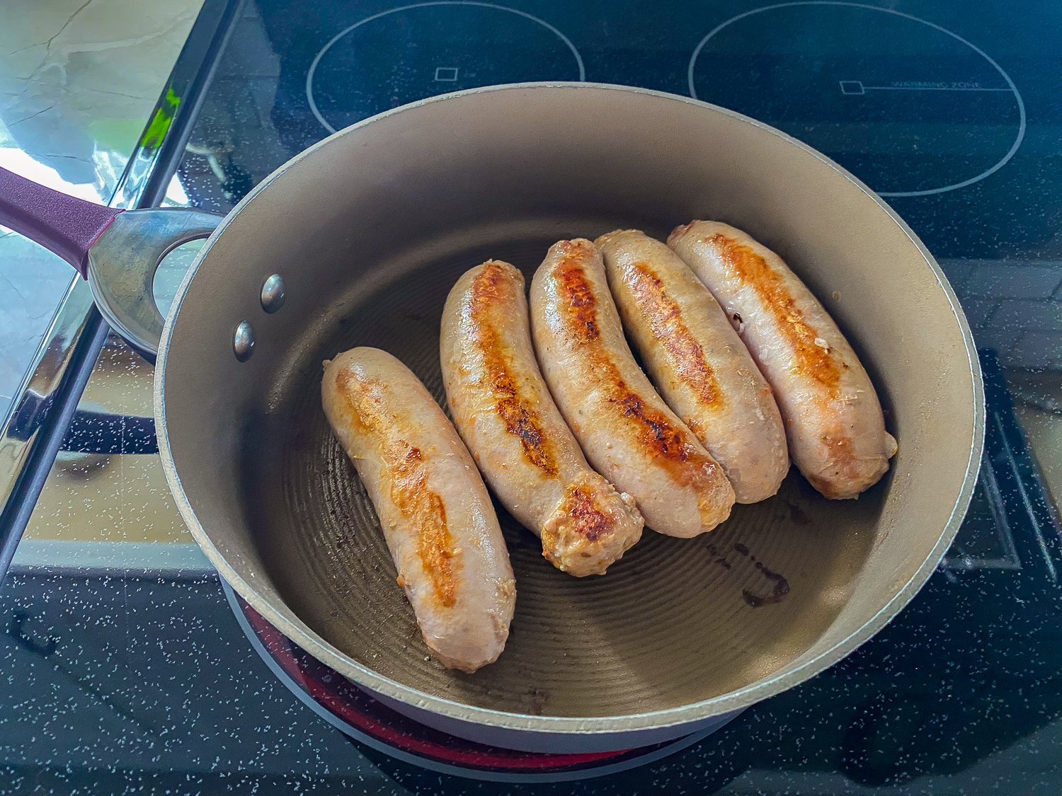 Italian Sausages being seared on a cast iron pan on a stove top.