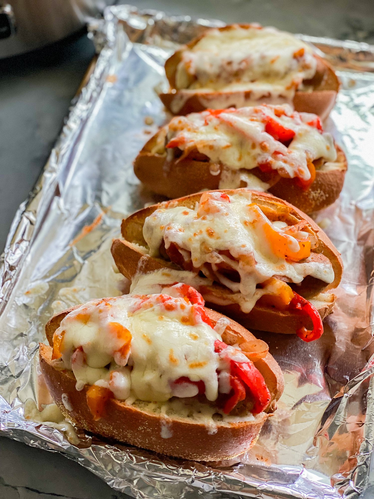 Italian Sausage and Pepper subs laying on a baking sheet covered in aluminum foil.