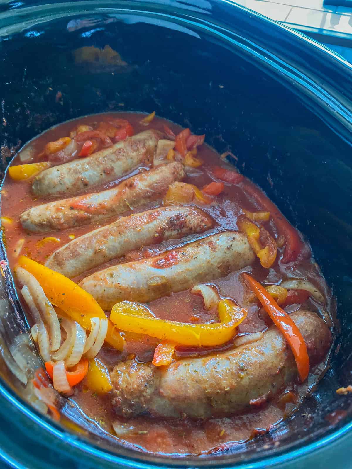 Picture of Italian Sausages simmering inside of an Instant Pot marinating with bell peppers, onions, and marinara sauce.