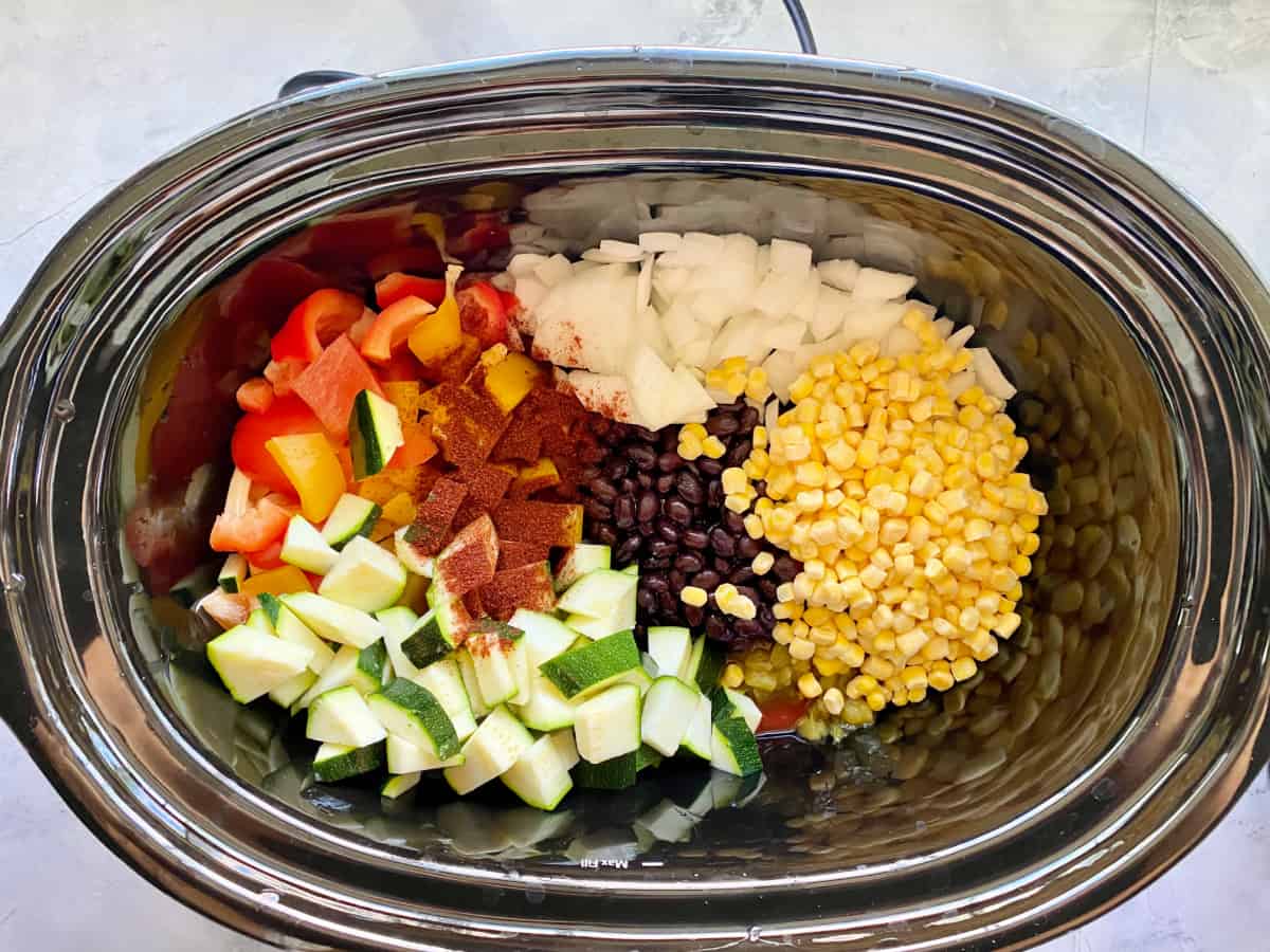 Black oval dish with onion, black beans, peppers, corn, and zucchini with spices.