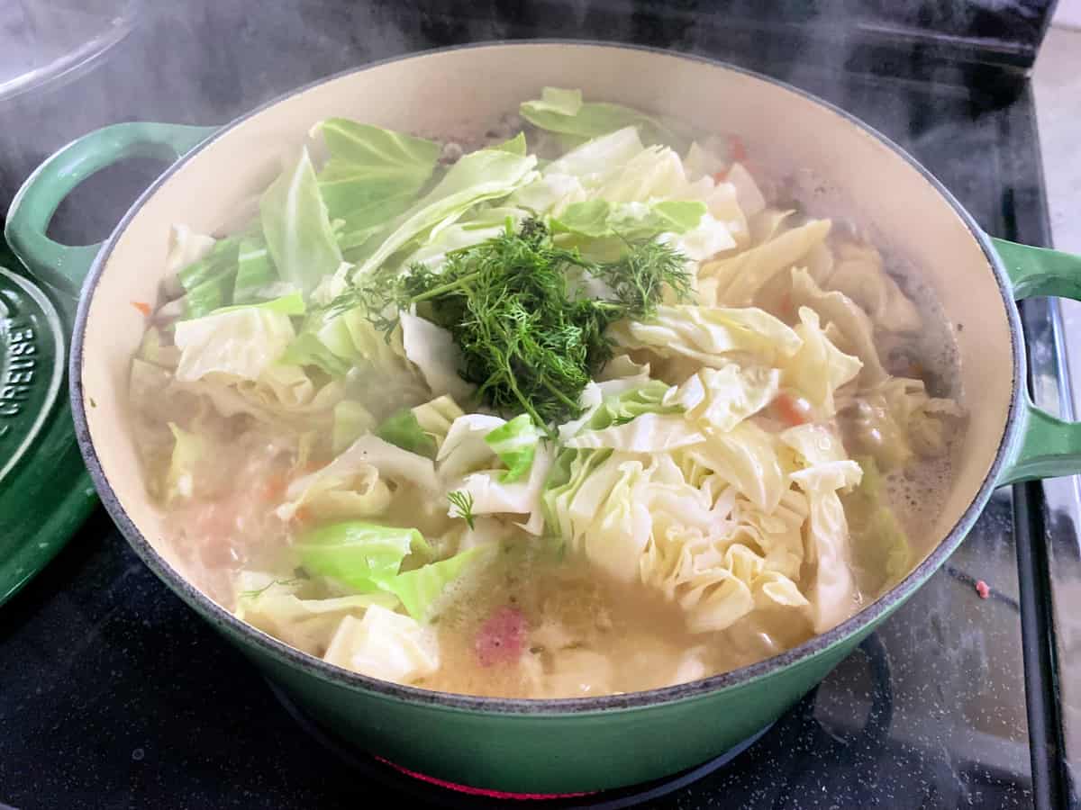 Green pot filled with cabbage, dill, and liquid on a stove top.