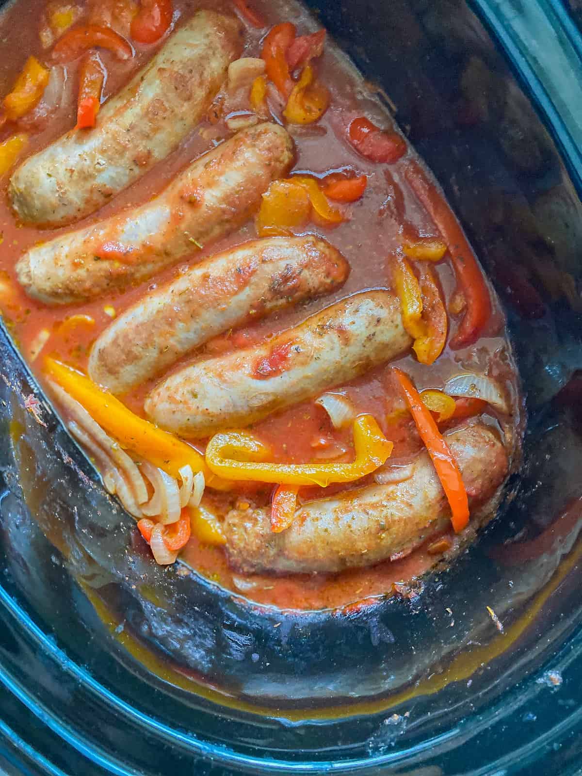 Picture of Italian Sausages inside of an Instant Pot marinating with bell peppers, onions, and marinara sauce, taken from a top angle.
