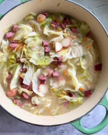 Large green pot filled with cabbage, sausage, potatoes, and broth on a marble countertop.