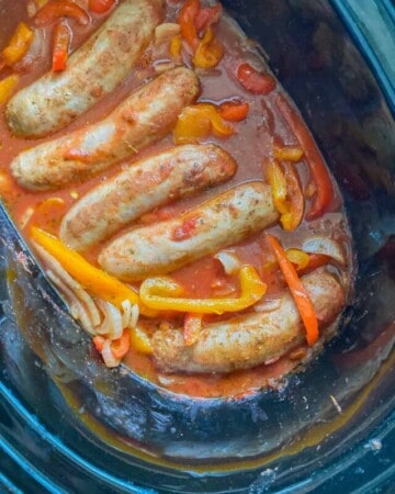 Picture of Italian Sausages inside of an Instant Pot marinating with bell peppers, onions, and marinara sauce, taken from a top angle.