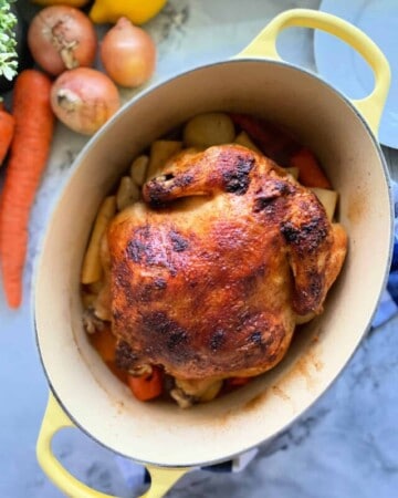Yellow oval baking dish with handles with a roasted whole chicken and vegetables inside.
