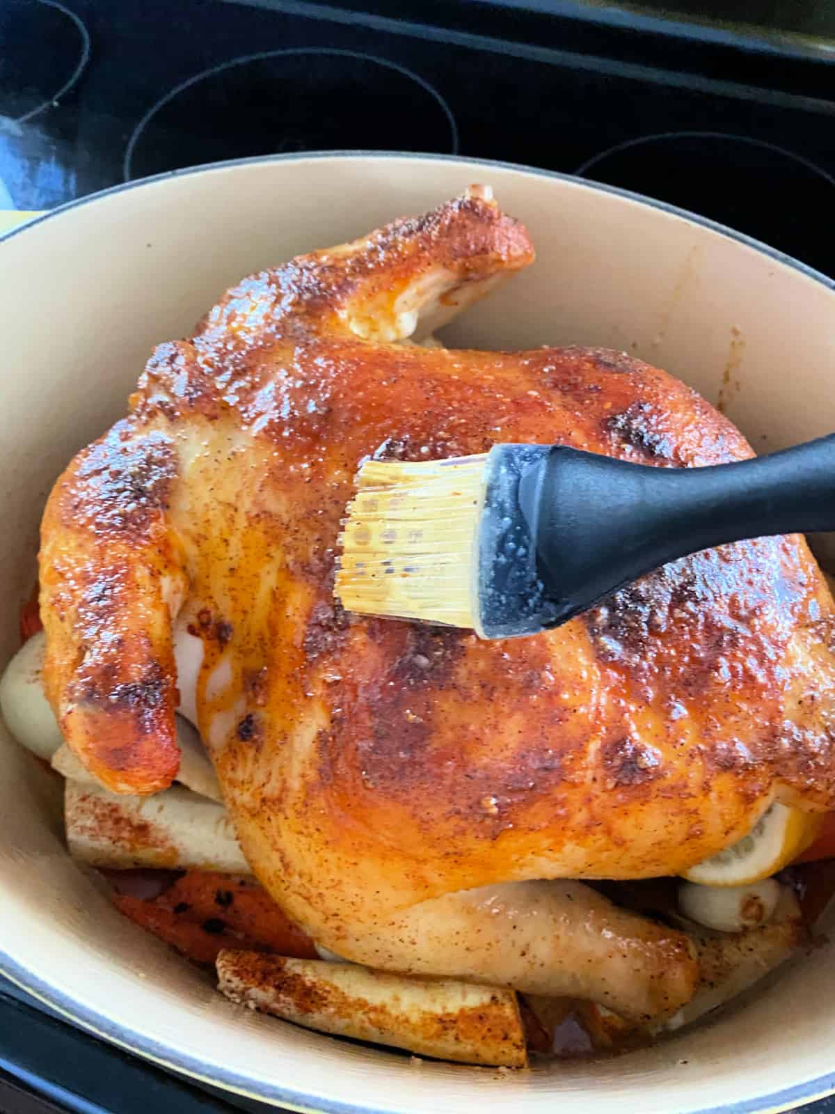 Black silicon brush basting butter on a whole chicken in a white pot.