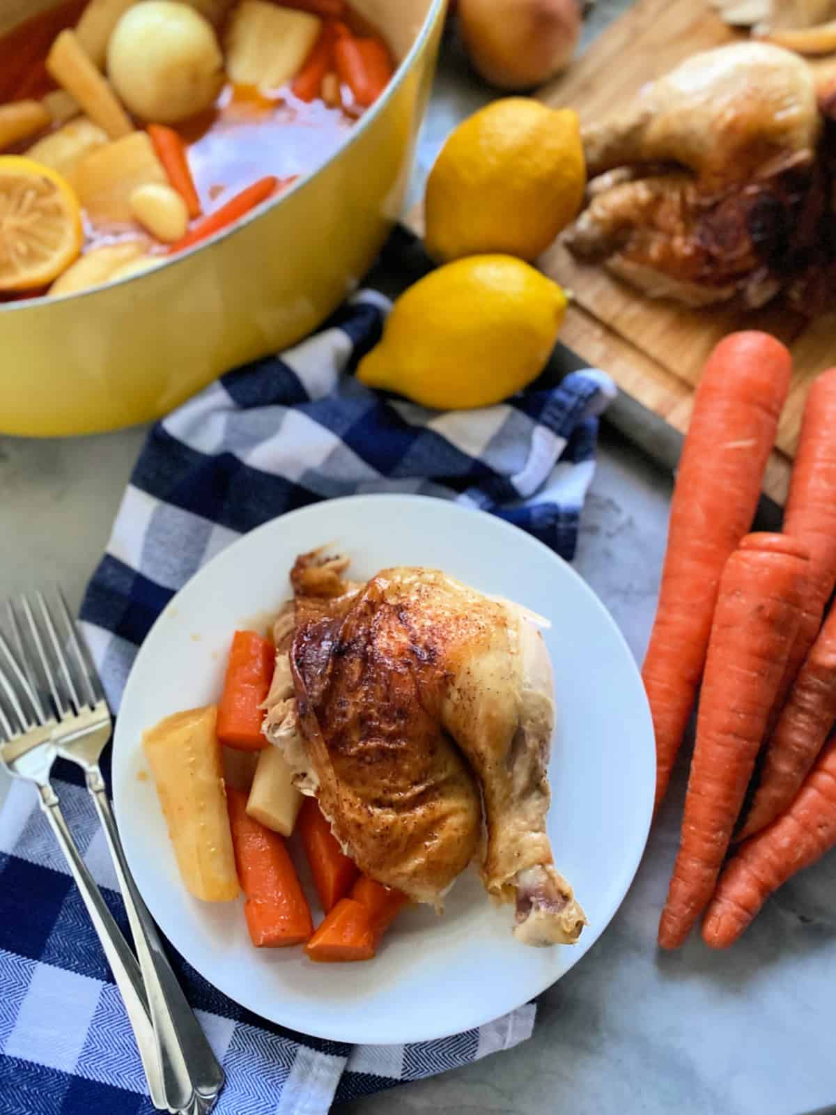 White plate filled with a quarter roasted chicken with carrots and parsnips with a yellow baking dish in the background.