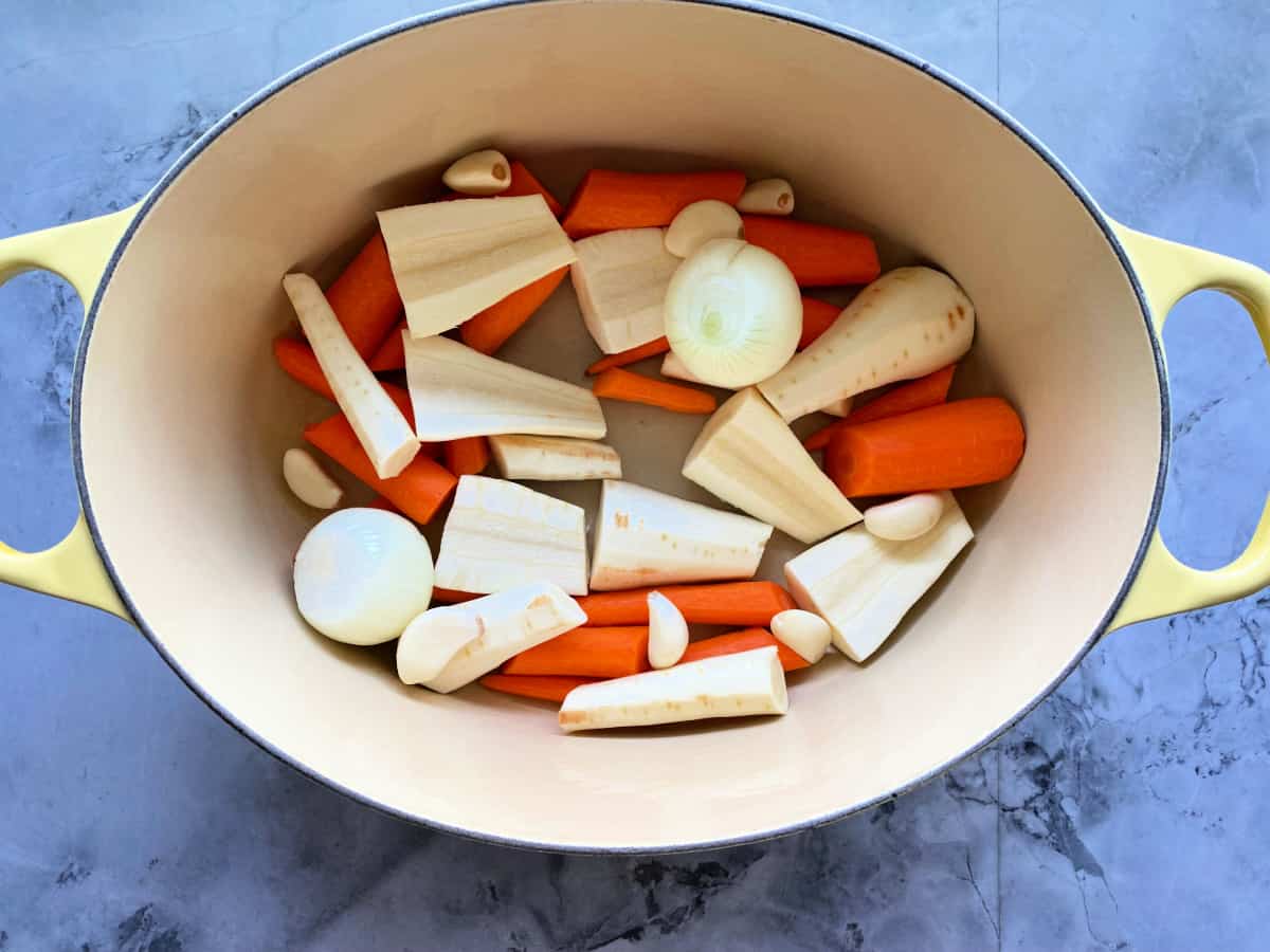 onions, carrots, and parsnips in a white and yellow oval pot.