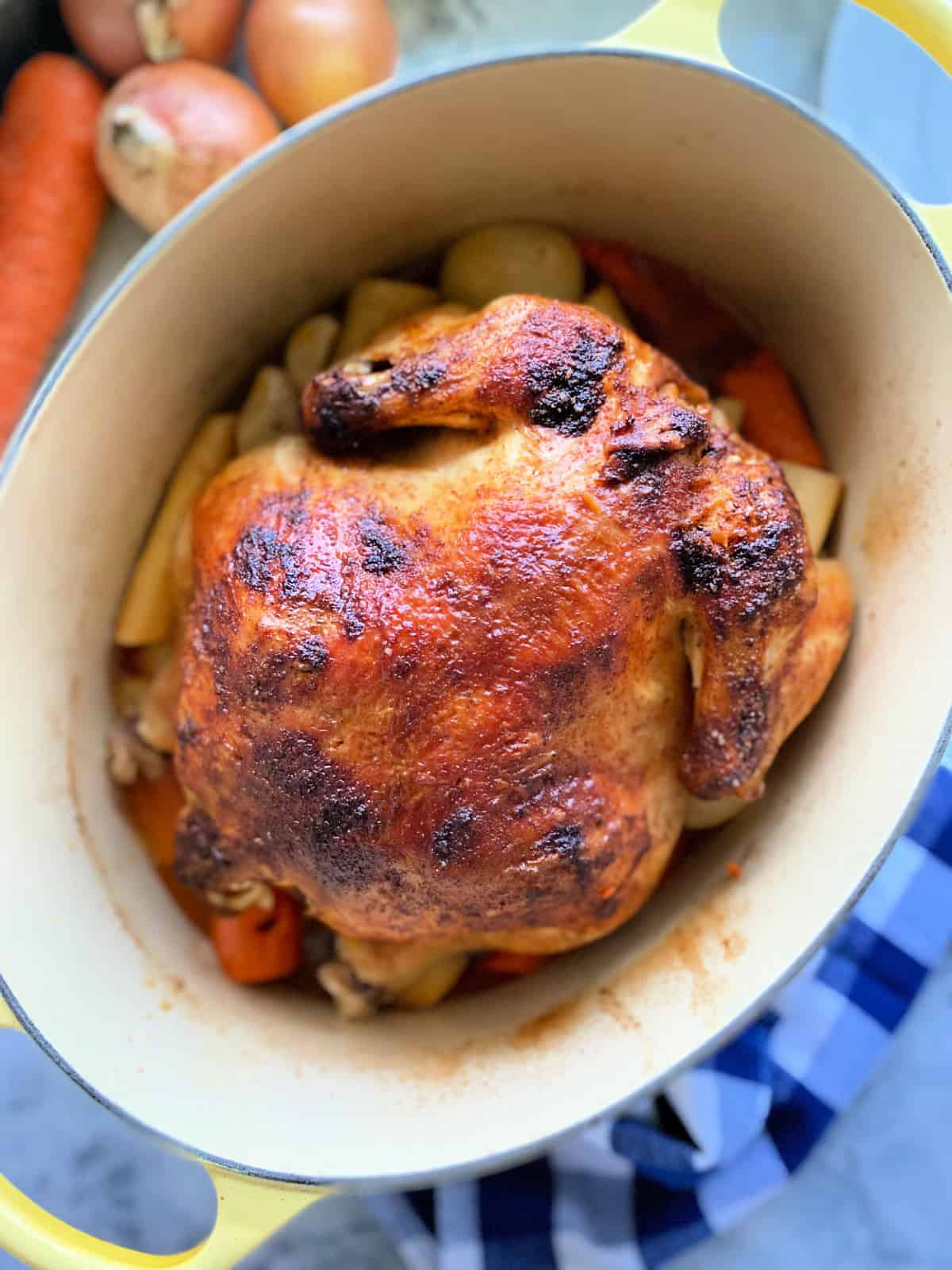 whole roasted chicken on top of vegetables in a white oval baking dish.