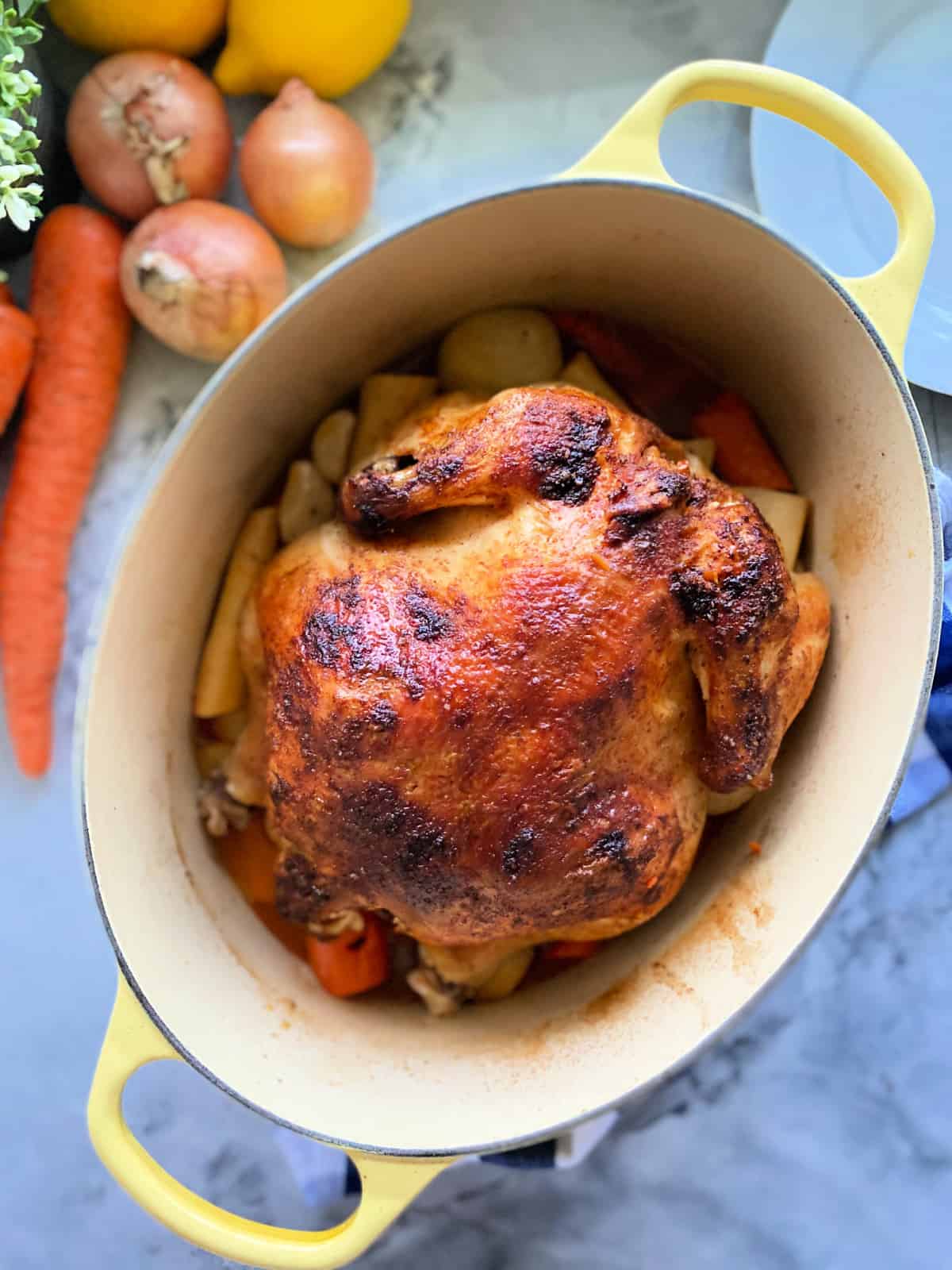 Yellow oval baking dish with handles with a roasted whole chicken and vegetables inside.