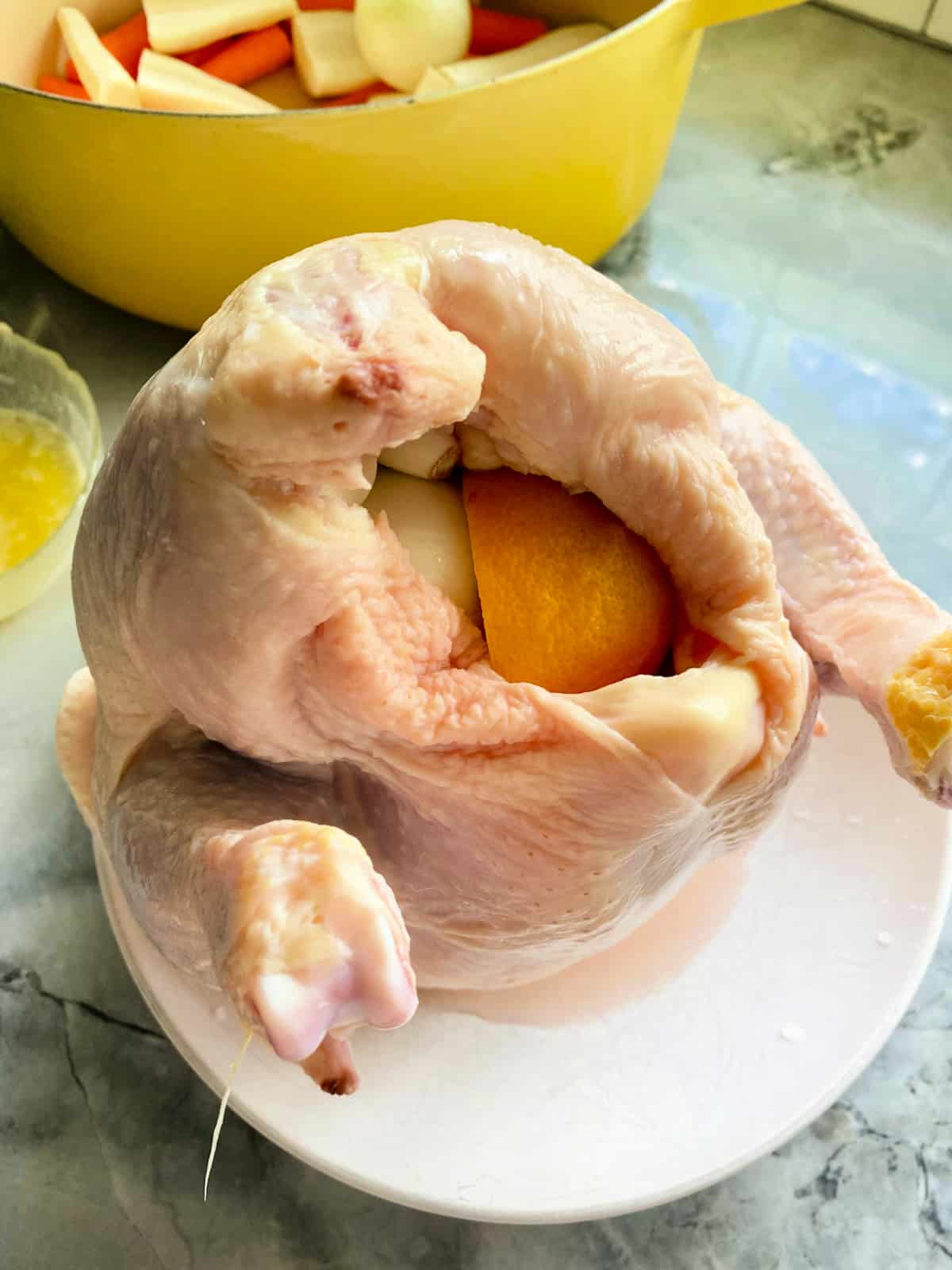 Whole chicken with lemon and onion in the cavity sitting on a white plate.