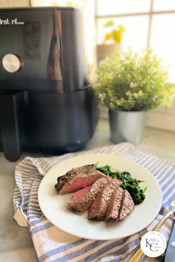 White plate on a white and blue striped cloth with an Air Fryer in the background and logo on the right corner.