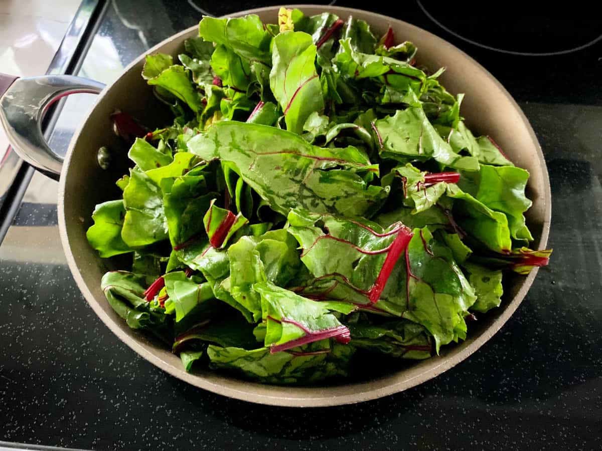 Chopped greens in a brown skillet on a black stove.