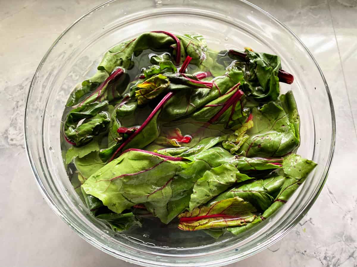 Glass bowl with greens soaking in water on a marble countertop.