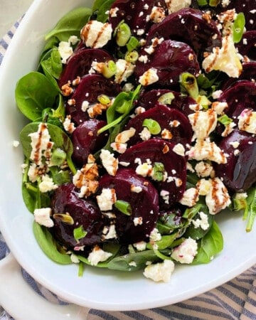 White oval dish filled with beets, feta, spinach, and balsamic drizzle.