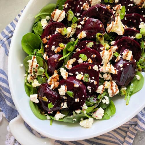 White oval dish filled with beets, feta, spinach, and balsamic drizzle.