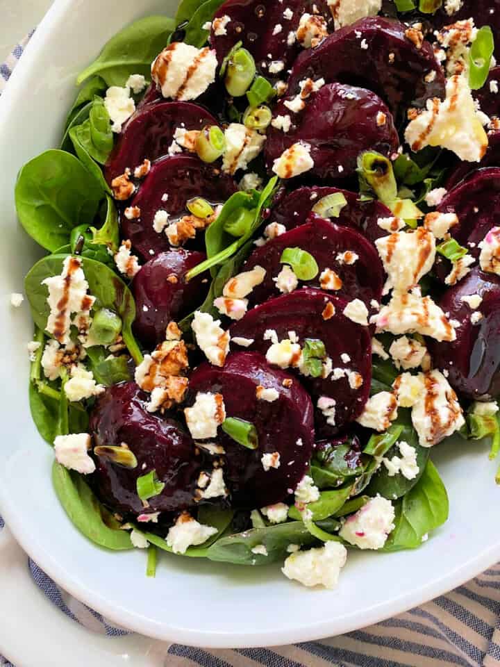 White oval dish filled with beets, feta, spinach, and balsamic drizzle.