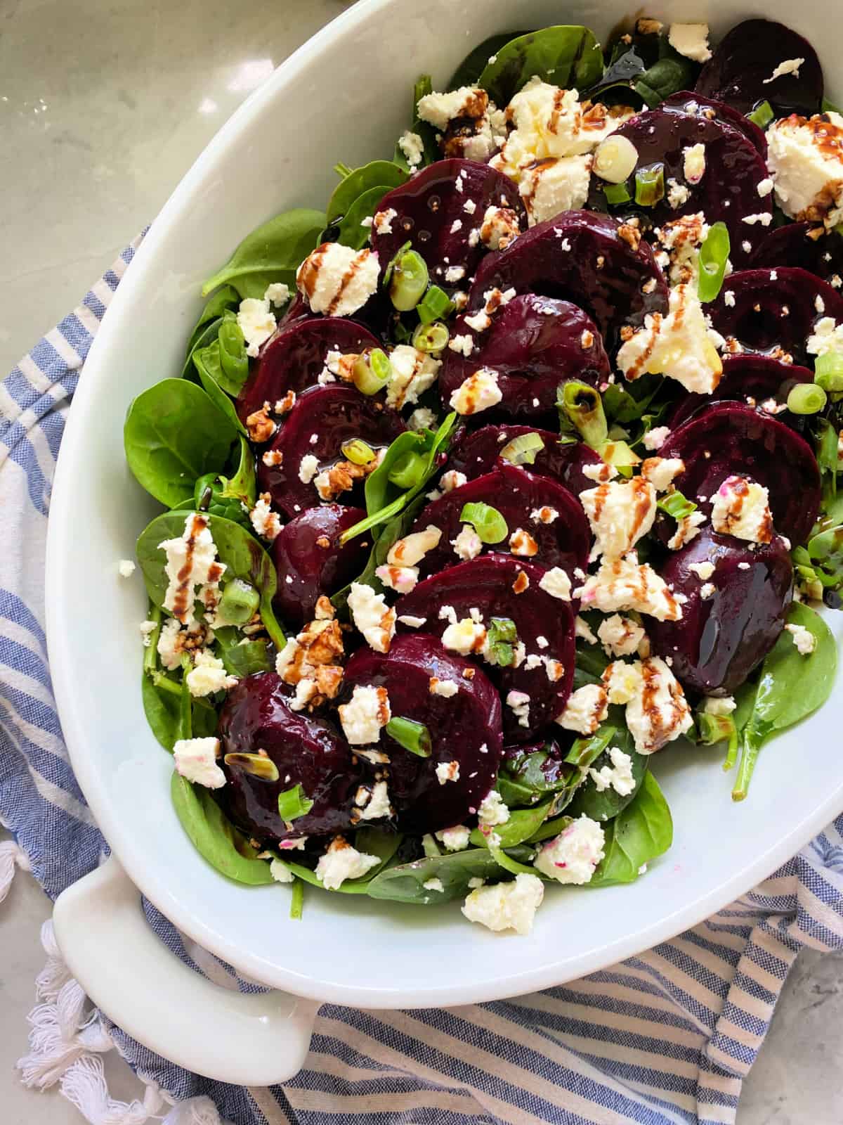 Oval bowl filled with feta, beets, and spinach on a white and blue striped cloth.