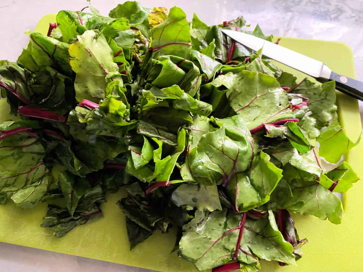 Chopped greens on a bright green cutting board with a knife.